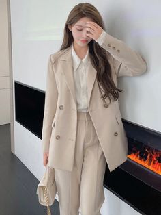 a woman standing in front of a fire place with her hand on her head and wearing a beige suit