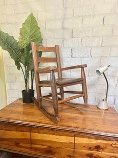 a wooden rocking chair sitting on top of a table next to a potted plant