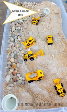 a plastic container filled with yellow toys on top of a sandy ground next to rocks