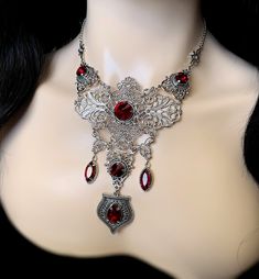 "This elegantly ornate necklace is made with light weight, antique silver tone filigrees and pendants, featuring romantic scrolls and beautifully balanced details. Its mesmerizing design is accented with dazzling dark ruby red glass crystals/jewels. Decorated portion is 6 1/2\" wide and 4 3/4\" tall in the very center. Necklace length is adjustable 15\"-18\" with soldered stainless steel cable chain, lobster clasp and extender. If you would like a different length, please send us a message. Matc Gothic Filigree Necklace For Wedding, Gothic Wedding Necklace With Filigree Detail, Red Metal Filigree Jewelry, Gothic Filigree Wedding Necklace, Gothic Wedding Necklaces With Jewels, Red Victorian Engraved Necklace, Victorian Red Engraved Necklace, Ornate Filigree Silver Bridal Necklace, Ornate Red Filigree Necklaces