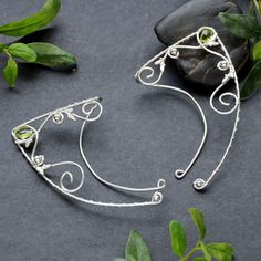 Elven ear cuffs/wraps made with sterling and fine silver and small peridot briolette.  The price is for a pair of cuffs. I can make variations with different stones, please message me. They are universal, lightweight and comfortable to wear - the shorter wire goes behind the ear and secures the wrap. You can slightly bend the wire to adjust it to your ear. Weight: 3,6 g 1 ear cuff Ear cuffs are totaly handmade and rhodium plated, so the silver does not tarnish. Handmade Adjustable Sterling Silver Ear Cuff, Handmade Adjustable Sterling Silver Ear Climbers, Handmade Adjustable Elven Jewelry, Elven Style Silver Ear Cuff As Gift, Adjustable Silver Wire Wrapped Ear Climbers, Adjustable Silver Elven Jewelry, Adjustable Silver Whimsical Ear Cuff, Whimsical Adjustable Silver Ear Cuff, Whimsical Adjustable Wire Wrapped Ear Cuff