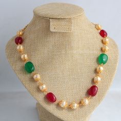 Explore the charm of this exquisite gold-plated necklace featuring captivating red and green semi-precious stones, complemented by semi-cultured pearls. The traditional shape of gold beads, reminiscent of South Indian and Maharashtrian jewelry, enhances the necklace's allure. Handcrafted with care, this 18-inch beauty is a fusion of sophistication and tradition. Multicolor Gemstone Bead Necklaces For Festive Occasions, Festive Multicolor Gemstone Bead Necklaces, Festive Red Pearl Chain Jewelry, Red Pearl Necklace For Celebration, Temple Jewelry Style, Festive Pearl Necklaces For Festivals, Gold Pearl Necklace With Gemstone For Festivals, Festive Gemstone Beaded Necklace, Festive Gemstone Necklace With Round Beads, Festive Red Pearl Necklace In Temple Jewelry Style