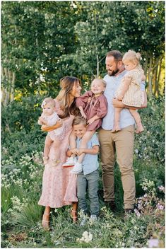 a family posing for a photo in the middle of some bushes and flowers with their children