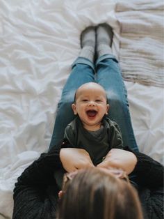 a baby laughing while sitting on top of a woman's leg in the air