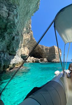 a woman sitting on the bow of a boat in clear blue water next to cliffs