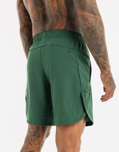 a man in green shorts with tattoos on his arm and back, looking down at the ground