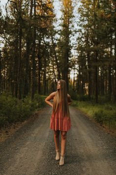 a woman standing on a dirt road in the middle of a forest with tall trees