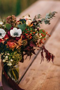 a vase filled with lots of flowers sitting on top of a wooden table covered in leaves