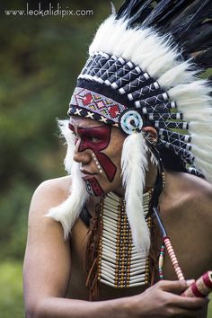 a native american man with his face painted red and white, holding a pipe in his right hand