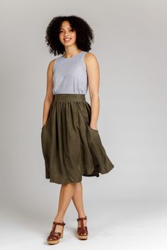 a woman standing in front of a white background wearing a green skirt and brown sandals