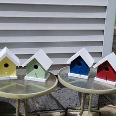 three small bird houses sitting on top of tables next to each other in front of a building