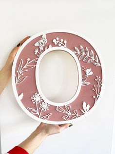 a person holding up a paper plate with flowers on it and the letter o cut out