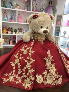 a teddy bear dressed in a red dress with gold embroidery on the skirt and neckline