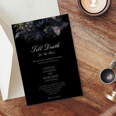 a black and white wedding card with flowers on it next to a candle, coffee cup and other items