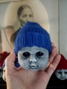 a person holding up a fake doll with a blue hat on