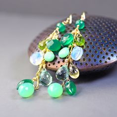 Long statement earrings in beautiful cool hues of green. These gold filled dangles are created with melange of drop, heart, pear and marquise briolettes of emerald green onyx, int green chalcedony and chrysoprase, olive green peridot, lemon yellow topaz and milky white opalite. All of shimmery gems are made into clusters swinging from gold filled bar chain. Top to bottom the earrings are 3 inches long. Long, dangly, flirty, fresh and  vibrant in color and very boho.  Attractive and eye catching Green Long Drop Earrings, Green Gemstone Dangle Earrings, Green Drop Jewelry With Gemstone Accents, Green Drop Earrings With Gemstone Accents, Green Teardrop Earrings With Gemstone Accents, Green Teardrop Jewelry With Gemstone Accents, Handmade Green Briolette Earrings, Green Teardrop Gemstone Accents Jewelry, Green Teardrop Gemstone Jewelry