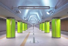 a long hallway with green columns and lights on either side of the corridor is lit by overhead lighting