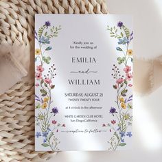 a wedding card with flowers and leaves on it next to a wicker table cloth