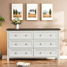 a white dresser with three pictures on the wall above it and a vase filled with flowers