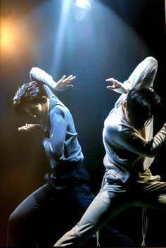 two men are dancing on stage with their hands in the air and one man is wearing a hoodie