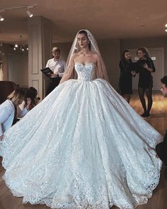 a woman in a white wedding dress standing on a wooden floor with people around her