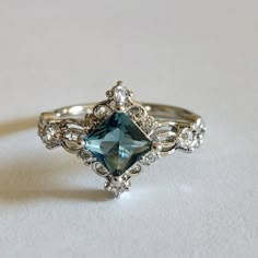 a fancy ring with an aqua blue stone surrounded by white diamonds on a plain surface