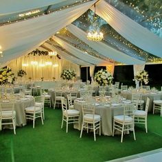 the inside of a tent with tables and chairs set up for a formal function in white linens