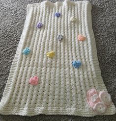 a crocheted blanket with hearts on it laying on the floor next to a pair of scissors