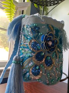 a blue purse with flowers and tassels hanging from it's side on a table