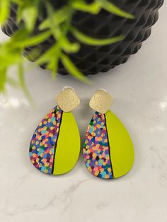 a pair of neon colored earrings sitting on top of a white table next to a potted plant