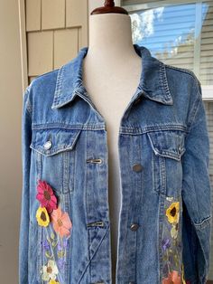 a denim jacket with flowers painted on the front and back, sitting on a mannequin