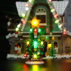 a lego lit christmas tree in front of a house with lights on it's roof