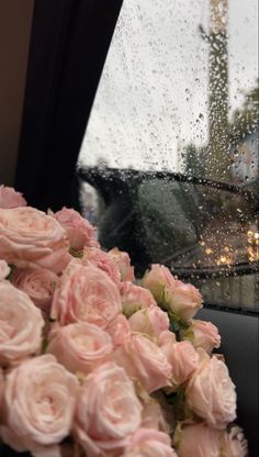 pink roses are sitting in the front seat of a car with rain drops on it