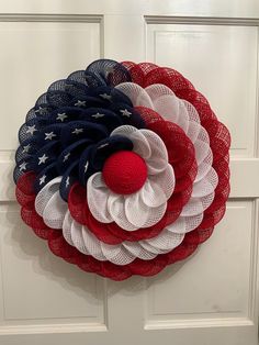 a patriotic wreath hanging on the front door with red, white and blue mesh flowers