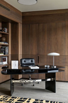 an office with wooden paneling and black leather chair, bookshelves, and desk lamp