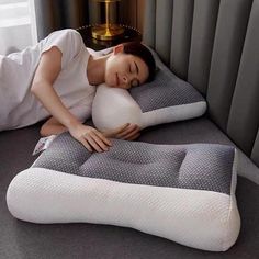 a woman laying on top of a pillow next to a bed with a lamp in the background