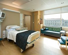 a hospital room with a bed, chair and television on the wall in front of large windows