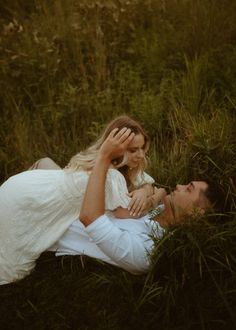 a man and woman laying on the ground in tall grass with their heads touching each other