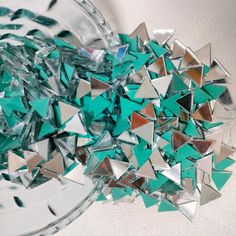 a glass bowl filled with lots of green and silver colored shards on top of a white surface