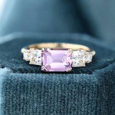 a pink sapphire and diamond ring sitting on top of a blue velvet cushioned box