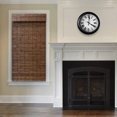 a clock on the wall above a fireplace in a room with hardwood floors and white walls