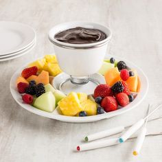 a white plate topped with fruit next to a cup of chocolate sauce on top of a table