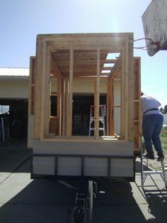 a man is working on the back of a tiny house being built with wooden framing