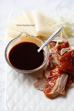 a white plate topped with meat and sauce next to an open jar of barbecue sauce