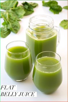 two glasses filled with green juice sitting next to each other