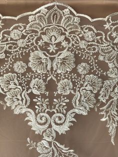 the back of a wedding dress with white lace and flowers on it, in front of a brown background