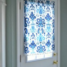 a blue and white door with a window covered in a roman blind that has an ornate pattern on it