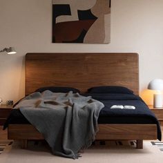 a bed with a wooden headboard and night stand next to a painting on the wall