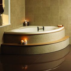 a bath tub sitting next to a window with candles on the floor in front of it