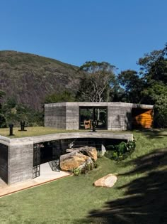 the house is made out of concrete and sits on top of a grassy hill with mountains in the background